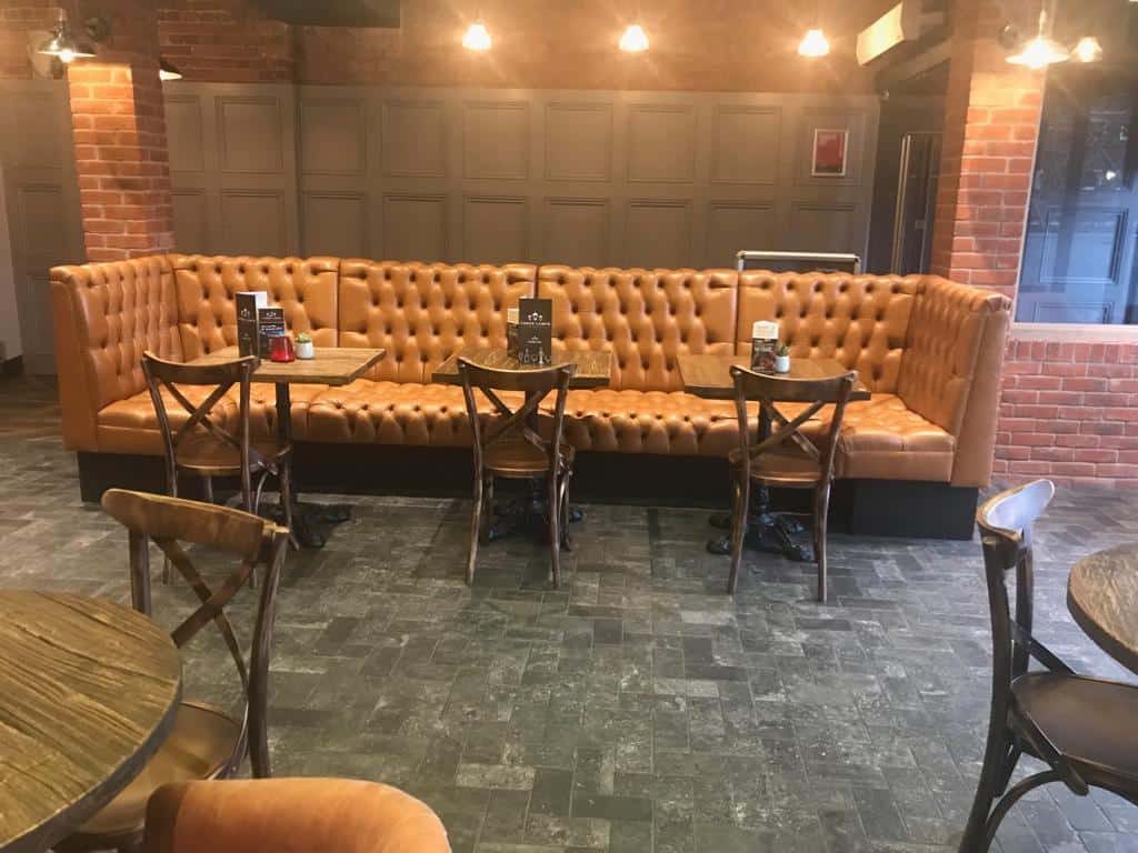 Deep-buttoned tan leather banquette seating along a brick wall in a bar